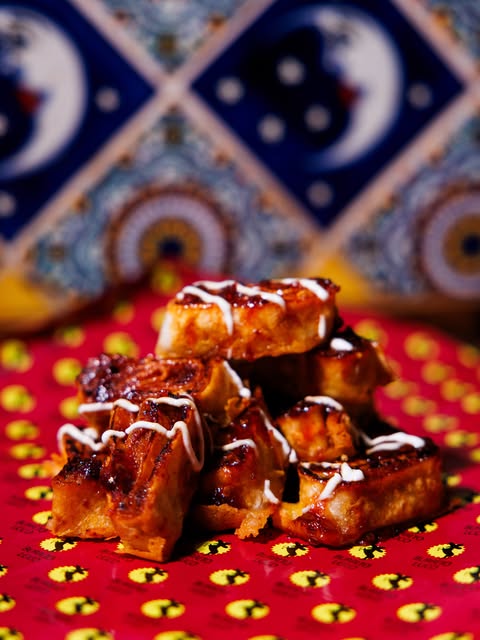 Golden dessert bites with dark and white sauce on pink Burrito Loco paper.