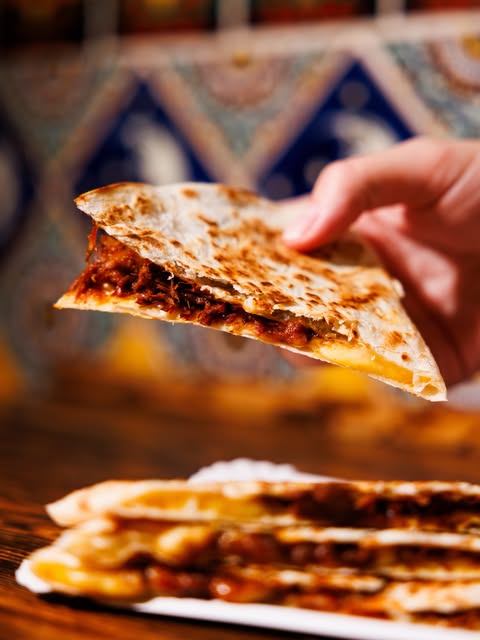 A hand lifting a toasted quesadilla triangle from a plate.